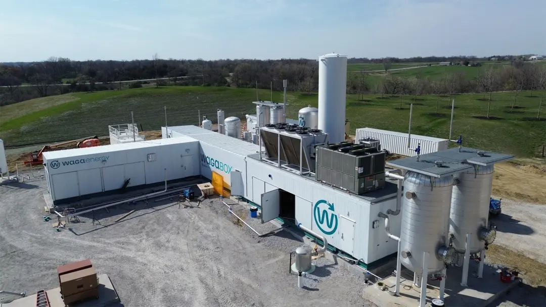 Aerial view of a WAGABOX® biogas upgrading facility installed at the Scott Area Landfill in Iowa. The installation includes modular processing buildings, vertical tanks, piping, and cooling equipment arranged on a gravel platform, surrounded by green fields. The facility is designed to upgrade landfill gas from a site producing less than 1,000 standard cubic feet per minute of biogas, with improvements to the gas collection system to enhance methane capture and reduce fugitive emissions.